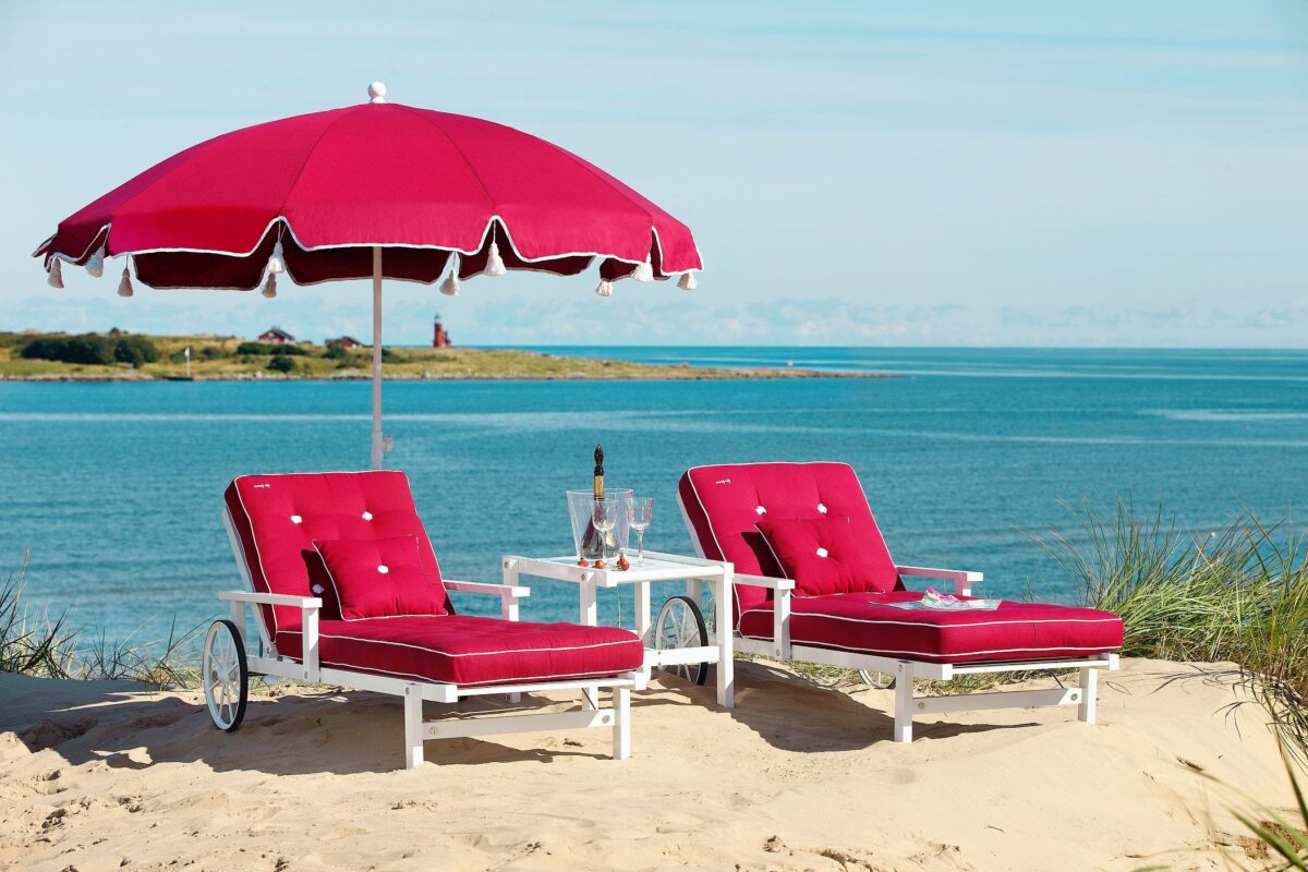 Sommar vid stranden med Fri Forms solsängar och parasoll i förgrunden.