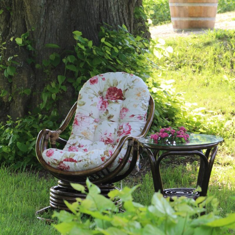 Pattaya rottingfåtölj i antikbets med blommig dyna i utemiljö.