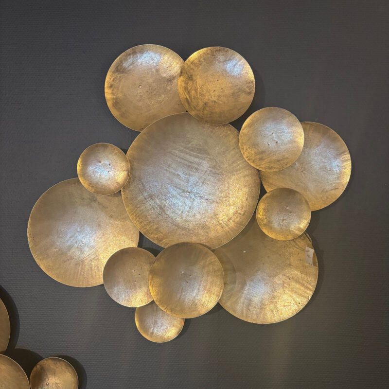 Väggdekoration, guldfärgade metallplättar i olika nivåer och storlekar.